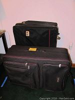 Full view of two large black luggage pieces, shows front zippered compartments, handles and design details.