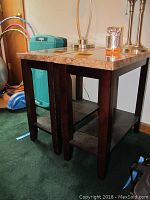 Two decorative end tables side by side with marble tops and dark wood legs and lower shelf, shot from front left angle.