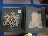 Photo of two Lenox ornaments in original green boxes; one a white snowflake and the other a white building with holiday scene