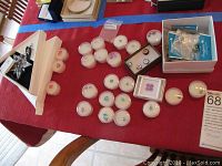 Overview of assorted loose precious stones in individual round plastic containers and several loose bracelet charms in a small open box placed on a table.