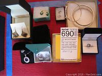 Overview of ten pieces of sterling silver jewelry including earrings, bangles, rings and pendants in original boxes and pouches, laid out on a red surface.