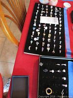 Two black velvet display trays on red surface holding approximately 48 rings on larger tray and 4 on smaller tray, plus one loose gold-tone band.