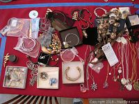 Wide view of assorted costume jewelry laid on red cloth including necklaces, bracelets, bangles, assorted beads, pendants and earrings.