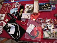 Wide view of assorted costume jewelry pieces on table including necklaces, bracelets, brooches, and watches with many displayed in open boxes or on fabric.