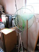 Photo showing three fishing rods with attached reels standing by a wall, accompanied by four different fish nets.