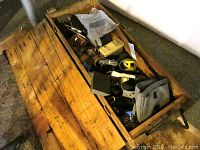 Wide view of wooden toolbox filled with tools and hardware items.