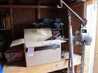 Cardboard box and shelf showing long drill bit extensions, toolbox, and chain come-along