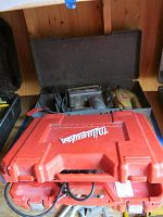 View of the lot showing the closed red Milwaukee rotary hammer carrying case and visible black and yellow power tools behind it.