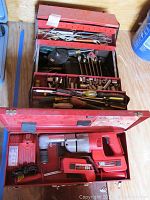 Open red metal toolbox displaying Milwaukee drill with 18V battery and right angle drive, alongside multiple trays filled with hand tools.