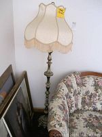 Front view of full floor lamp showing ornate brass-colored stand and scalloped fabric lampshade with beige fringe some minor wear visible on shade.