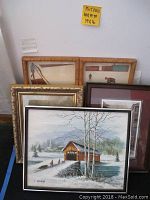 Five framed artwork pieces arranged against a wall showing variety in size and frame style, with sizes noted on a sticky note