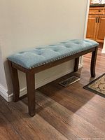 Full side view of bench showing teal upholstered seat, nailhead trim, and dark wood legs