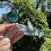Hand holding stained glass cricket and snail plant stake outdoors