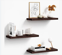 Stock image showing three brown wood floating shelves mounted on a white wall with decorative items