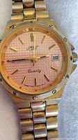 Front view of SJT watch showing pink dial, date window, gold baton markers