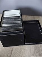 Closed black faux-leather box filled with sleeved discs, lid alongside