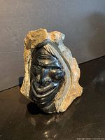 Front view of carved black stone face within raw stone