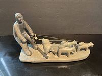 Oblique view of entire soapstone sled team with hunter, dogs, and seal