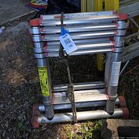 Front view of collapsed aluminum telescoping ladder with red end caps and rope attached