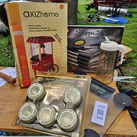 Lot overview showing boxed popcorn maker, halogen light kit, knife set box, plastic pitcher