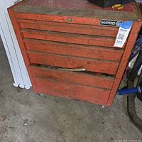 Front view of red Matco rolling tool chest with six drawers, casters and visible wear, partial drawer contents visible