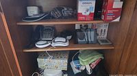 Cabinet shelves holding blood pressure monitor, boxes, phone base, sound machines, digital photo frame and accessories