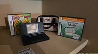 Front view of black Nintendo DS console open, two game boxes, carrying case