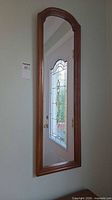 Mirror mounted on wall showing full view, oak wood frame and arched top visible