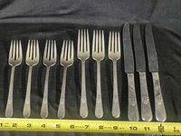 Six dinner forks and three dinner knives laid out beside ruler