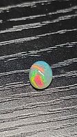 Oval opal on textured black background highlighting play-of-color