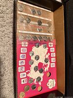 Open box showing display board with coins and plastic strips