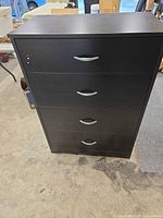 Full front view of black 4-drawer dresser showing handles and overall wear