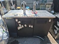 Front view of True kegerator showing twin tap towers, four taps, stainless top, black cabinet, brand badges