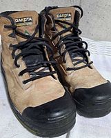 Front angled view of both boots showing tan leather uppers, black toe guards, laces and branding