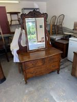 Front view showing dresser with mirror attached, carved crest, three drawers, brass pulls