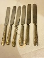 Front view of six silver-plated butter knives showing handle ornamentation and blades
