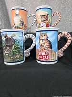 Front view of four Danbury Mint Comical Cats mugs showing illustrations and striped handles