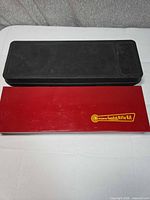 Closed red rifle cleaning kit case beside outer black lid