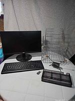 Monitor, keyboard, stackable wire trays and black mesh tray on table