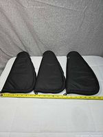 Three black padded gun cases side by side with measuring tape indicating length