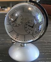 front view showing dual clock dials within glass globe on metal base