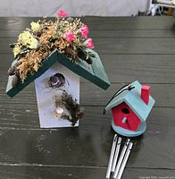 Large white and green birdhouse with florals beside smaller teal and red wind-chime birdhouse