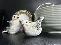 Two porcelain bird figurines, gold-trim saucer, ribbed bowl in background