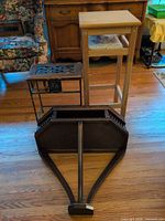 All three pieces laid out on floor: dark magazine rack, light wood stand, black metal stand