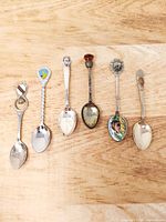 Overview of six souvenir teaspoons laid out side by side