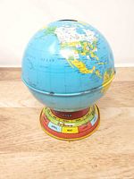 Full view of metal globe coin bank on base