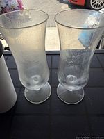 Two clear tumblers with flared rims on black surface