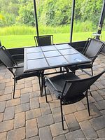 Square patio table with four matching chairs on paver patio