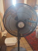 Front view of Lasko pedestal fan showing grille, blades, and logo