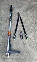 All three Fiskars tools laid on concrete: stand-up weeder, loppers, pruner